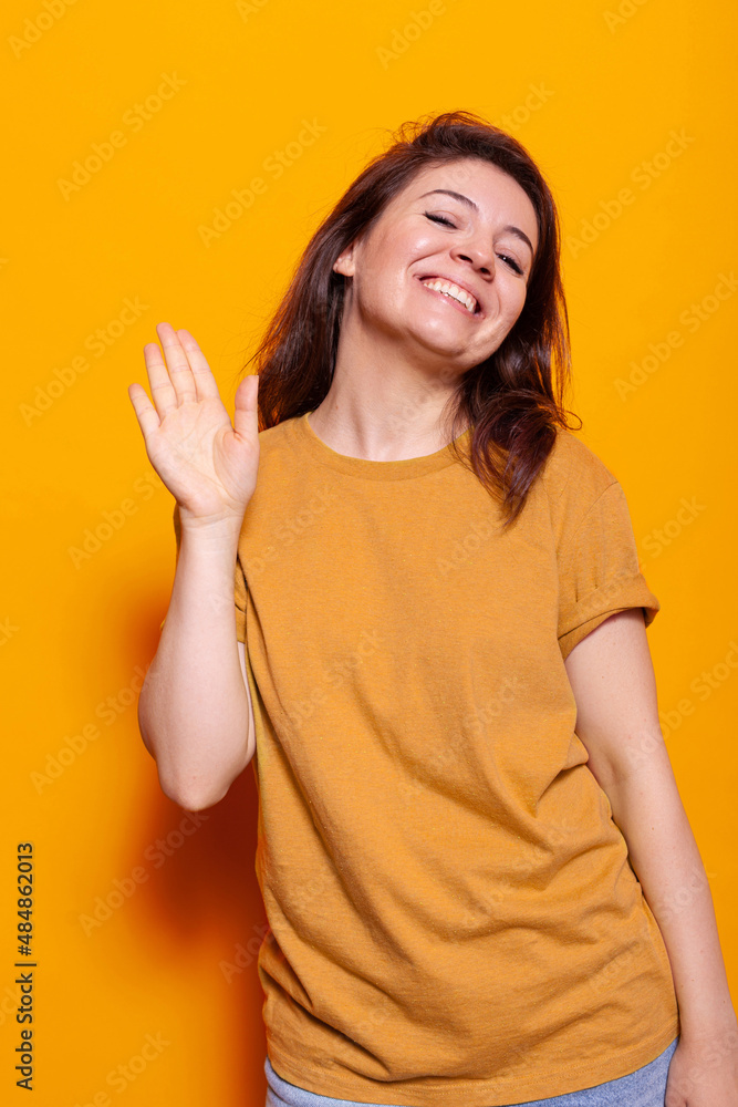 Smiling woman waving with palm at camera in studio, having fun. Cheerful person doing salute gesture to greet people and waving with hand. Young adult being friendly, doing greeting symbol Smiling woman waving with palm at camera in studio, having fun. Cheerful person doing salute gesture to greet people and waving with hand. Young adult being friendly, doing greeting symbol