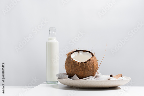 Una botella de leche de coco y un coco abierto sobre una mesa blanca