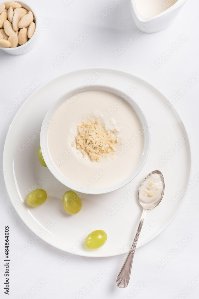 Crema de almendras, sopa fría española. Ajo blanco de Málaga con almendras y uvas en un recipiente blanco sobre una mesa blanca. Vista superior Crema de almendras, sopa fría española. Ajo blanco de Málaga con almendras y uvas en un recipiente blanco sobre una mesa blanca. Vista superior