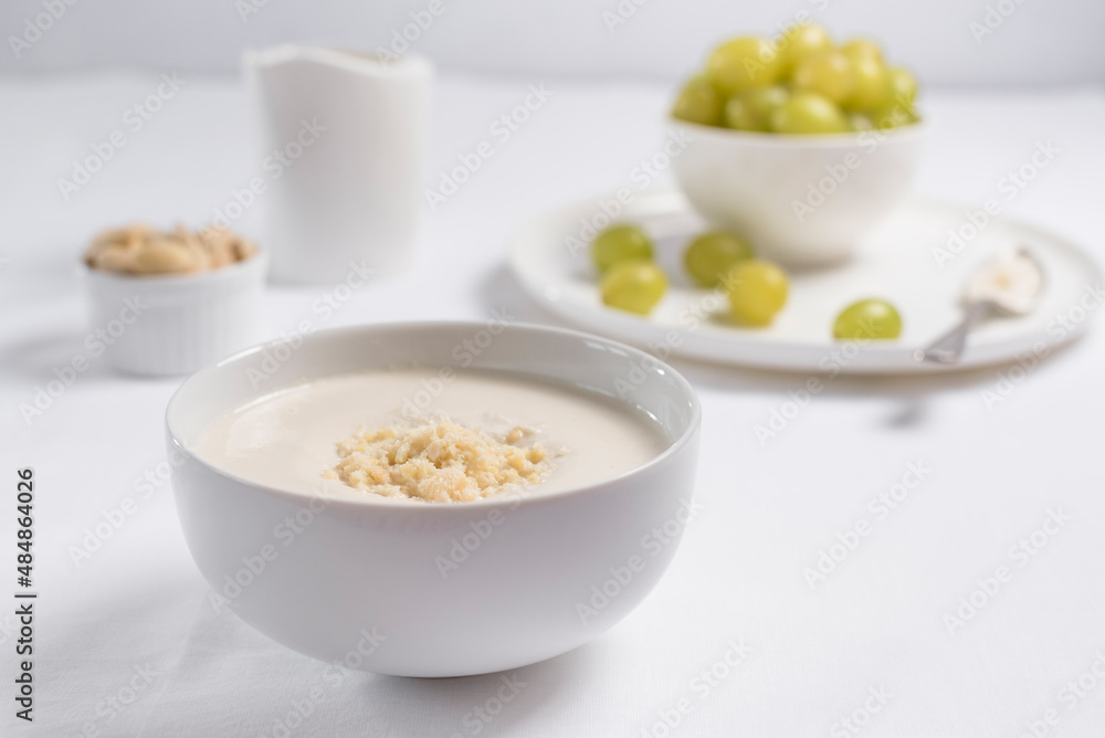 Crema de almendras, sopa fría española. Ajo blanco de Málaga con almendras y uvas en un recipiente blanco sobre una mesa blanca Crema de almendras, sopa fría española. Ajo blanco de Málaga con almendras y uvas en un recipiente blanco sobre una mesa blanca