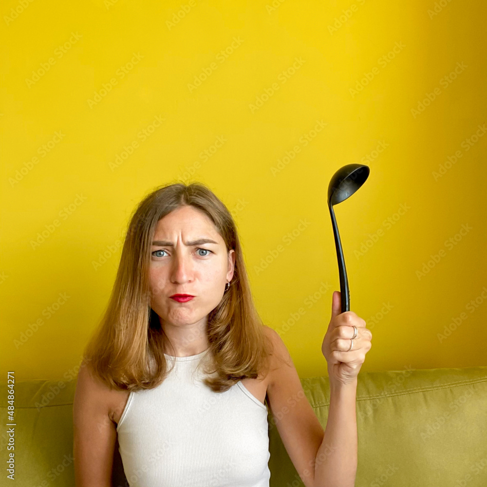 Young housewife isolated on yellow background holding ladle Young housewife isolated on yellow background holding ladle
