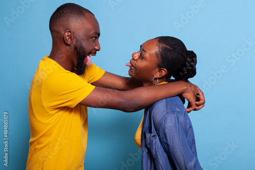 Playful lovers hugging and sticking tongue out at each other. Girlfriend and boyfriend fooling around with goofy gesture, expressing happiness and corny romance. Positive couple having fun. photo