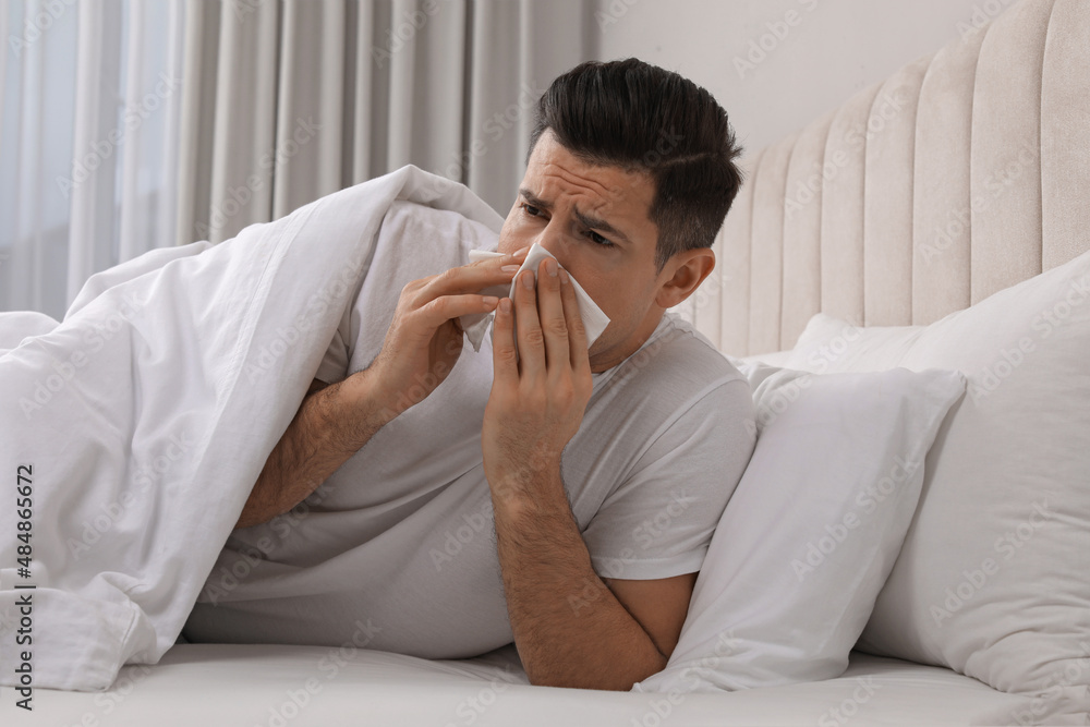 Sick man with tissue suffering from cold in bed at home Sick man with tissue suffering from cold in bed at home