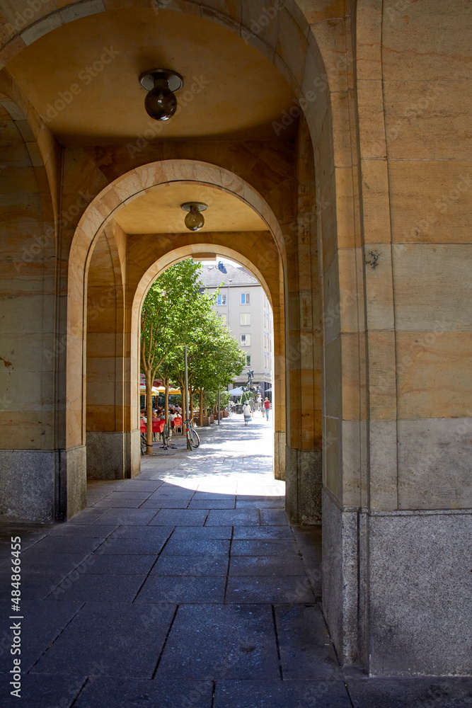 Dresden, Germany, August 20, 2021. Arch, road under buildings with row of trees behind. Building with marble on its walls.