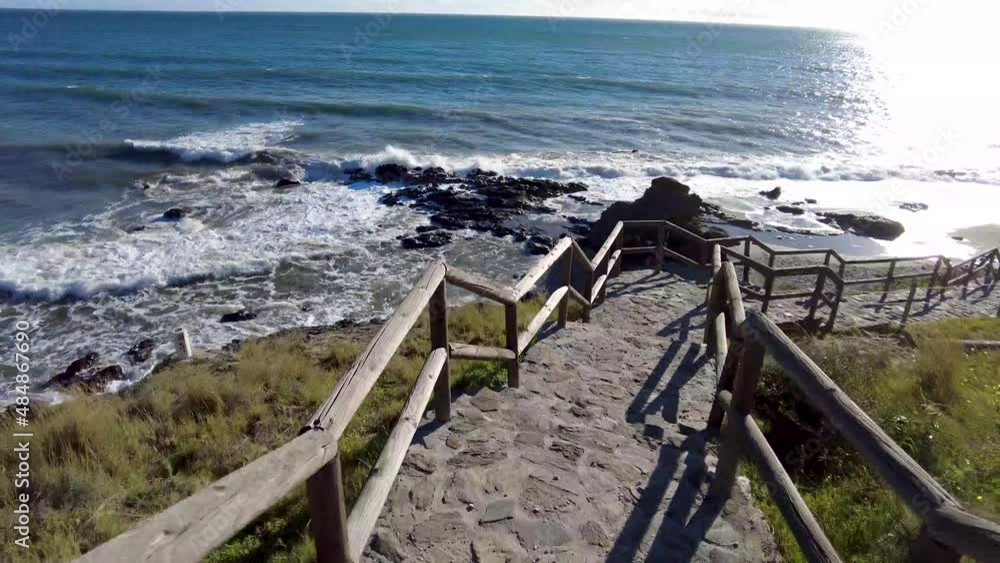 Walking down the stairs to the beach in Nerja Spain. Big waves crashing in on the black rocks on the beach. Sunny day on the beach in the southern part of Spain. Healthy walk to the beach. Walking down the stairs to the beach in Nerja Spain. Big waves crashing in on the black rocks on the beach. Sunny day on the beach in the southern part of Spain. Healthy walk to the beach.