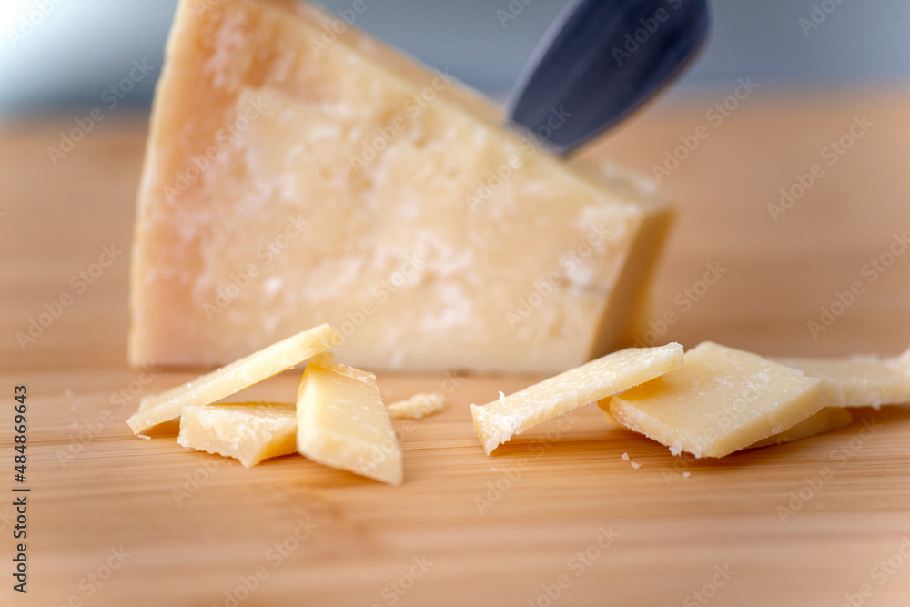 piece of parmesan cheese with slices on wooden cutting board in natural light piece of parmesan cheese with slices on wooden cutting board in natural light