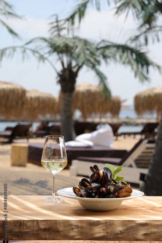 Mussels in a white plate served with a glass of white wine at the beach