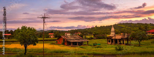 Traditional Indian village house and temple surrounded by green grass and beautiful sunset view. photo