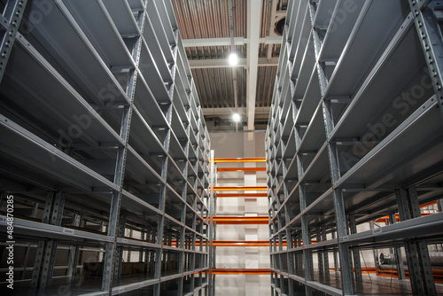 empty gray and high shelves of a large warehouse lit by lamps