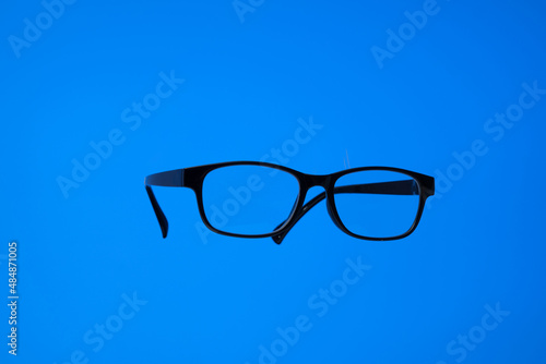 Black plastic frame eyeglasses. Close up studio shot, isolated on blue background, no people