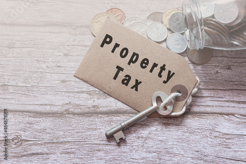 Property tax text on brown tag with a key and coins background on wooden desk photo