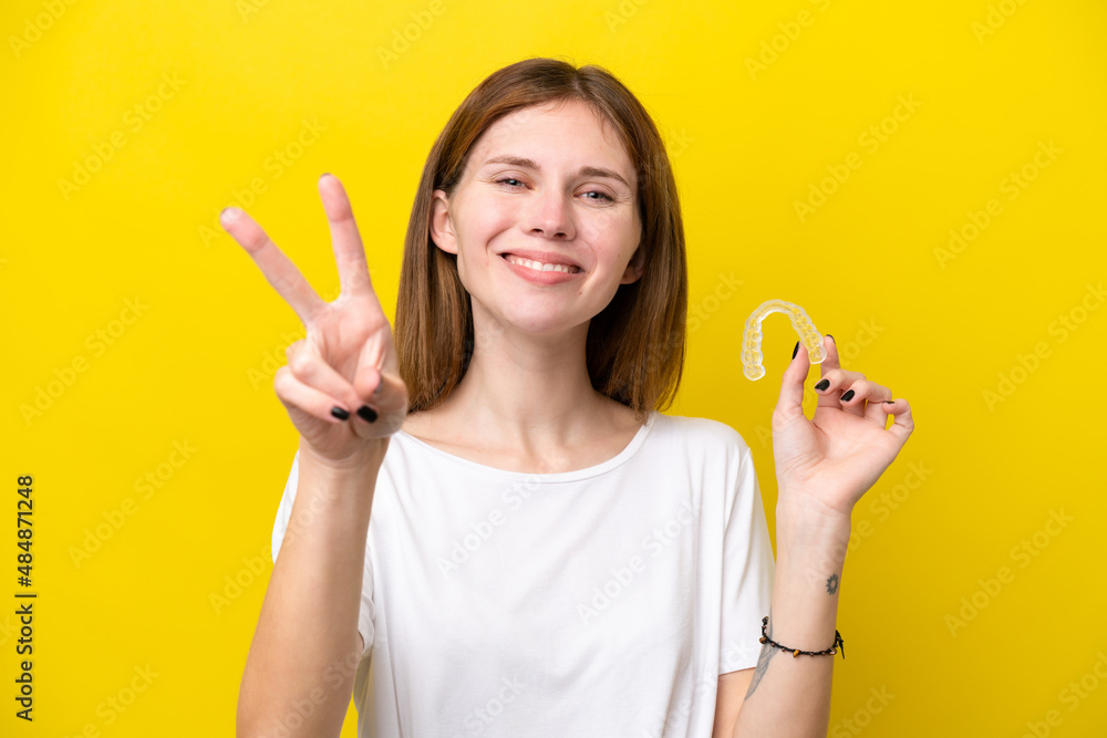 Young English woman holding invisible braces smiling and showing victory sign Young English woman holding invisible braces smiling and showing victory sign