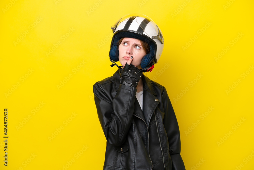 Fototapeta premium Young English woman with a motorcycle helmet isolated on yellow background having doubts