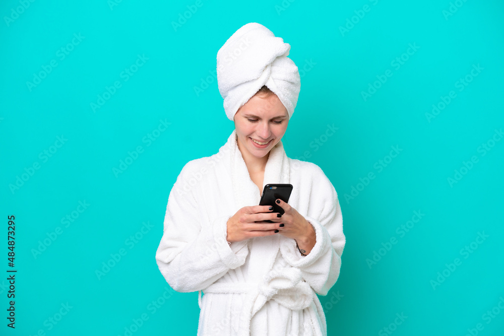 Young woman in a bathrobe isolated on blue background sending a message with the mobile Young woman in a bathrobe isolated on blue background sending a message with the mobile