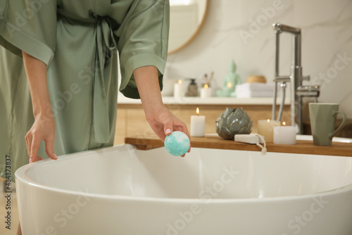 Young woman holding bath bomb over tub in bathroom, closeup