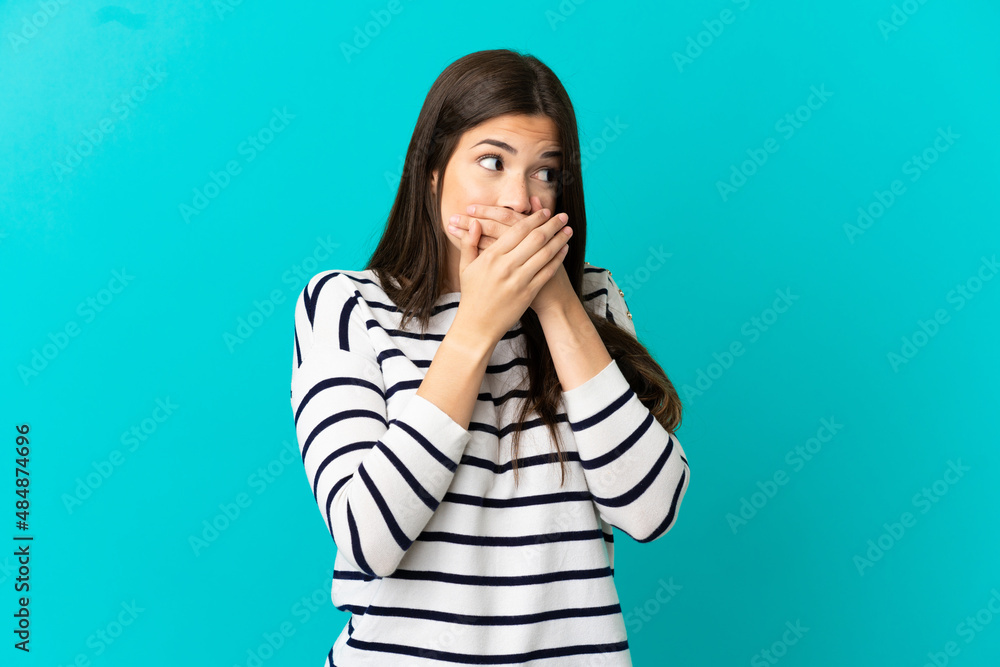 Teenager Brazilian girl over isolated blue background covering mouth and looking to the side Teenager Brazilian girl over isolated blue background covering mouth and looking to the side
