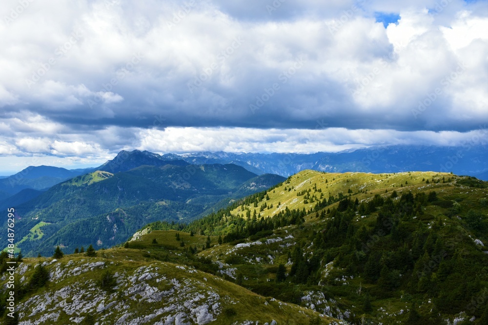 View of Julian alps in Gorenjska, Slovenia and Ratitovec mountain range with forest covering the base and meadow at the top