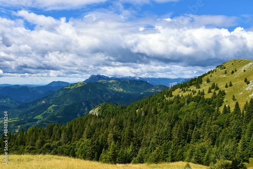 View of Julian alps in Gorenjska, Slovenia and Ratitovec mountain range with forest covering the base and meadow at the top