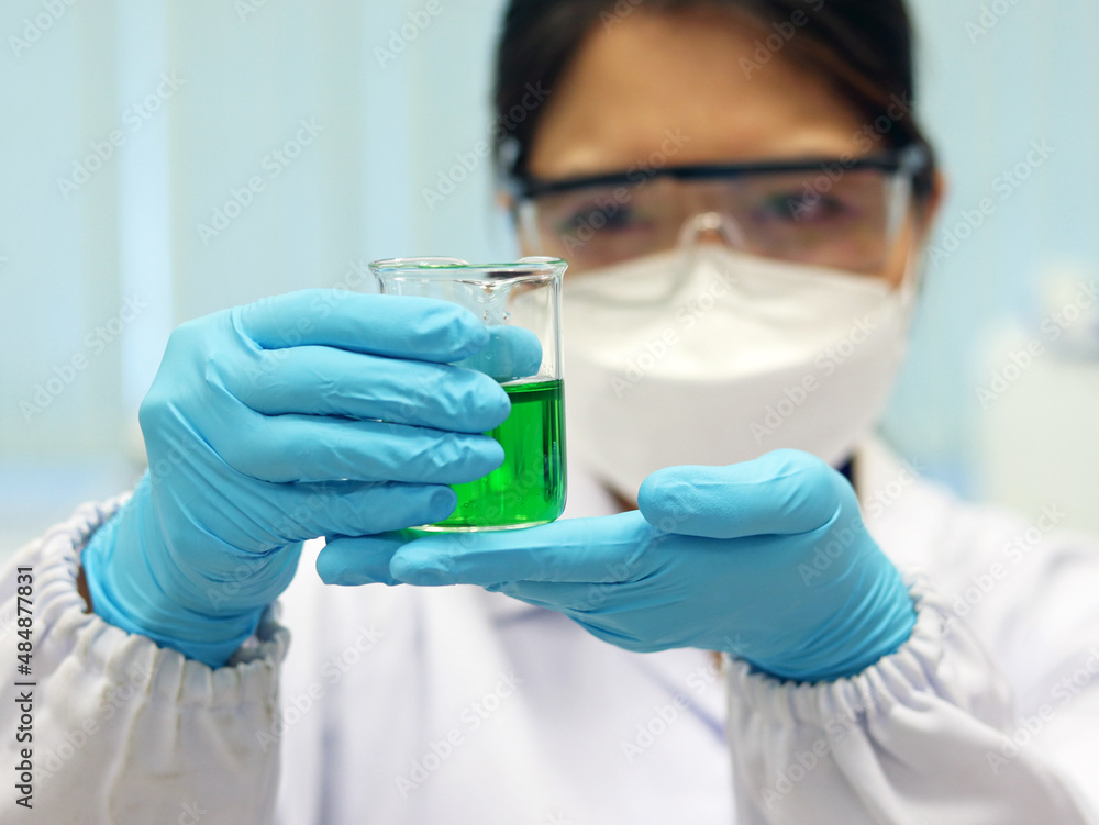 The scientist wear PPE and hold a beaker laboratory, with green solvent