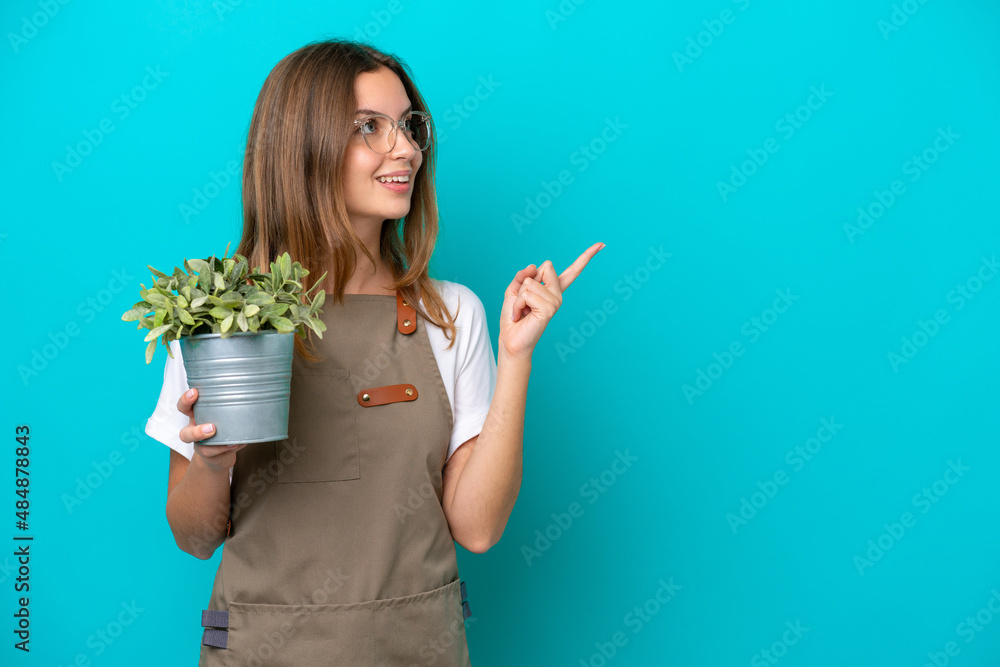 Young caucasian gardener woman holding a plant isolated on blue background intending to realizes the solution while lifting a finger up Young caucasian gardener woman holding a plant isolated on blue background intending to realizes the solution while lifting a finger up