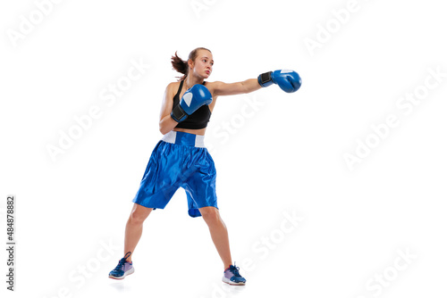 Dynamic portrait of young girl, professional boxer practicing in boxing gloves isolated on white studio background. Concept of sport, studying, competition