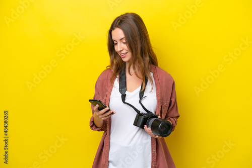 Young photographer caucasian woman isolated on yellow background sending a message with the mobile