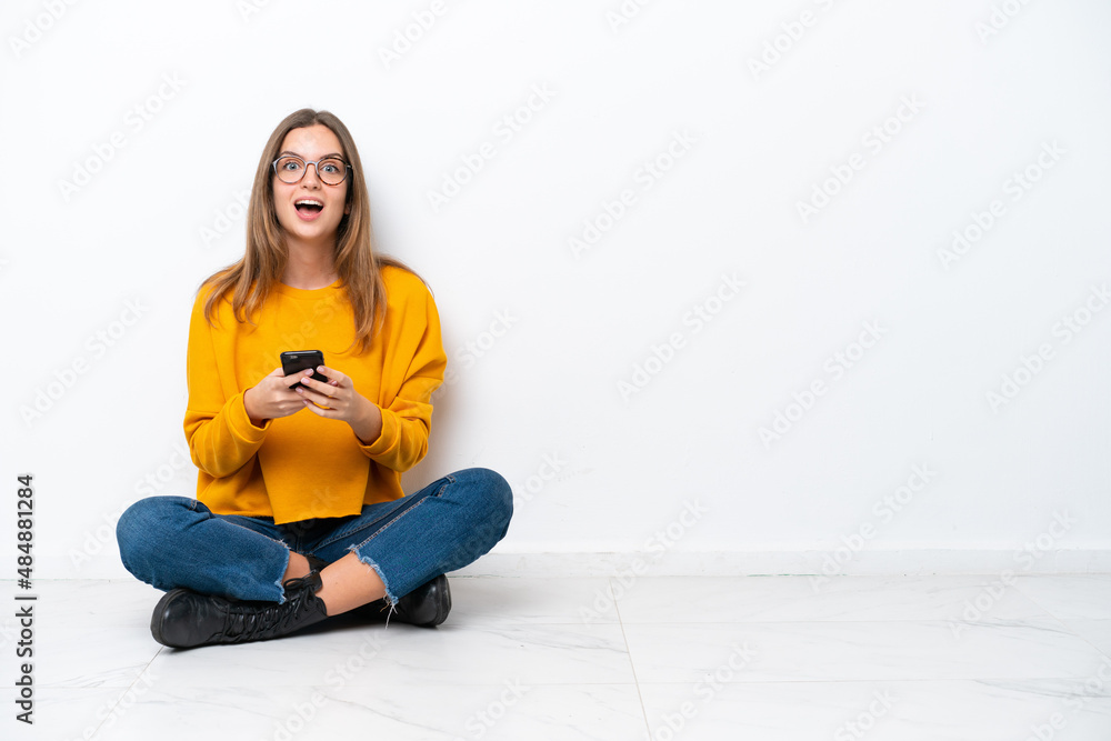 Young caucasian woman sitting on the floor isolated on white background surprised and sending a message Young caucasian woman sitting on the floor isolated on white background surprised and sending a message