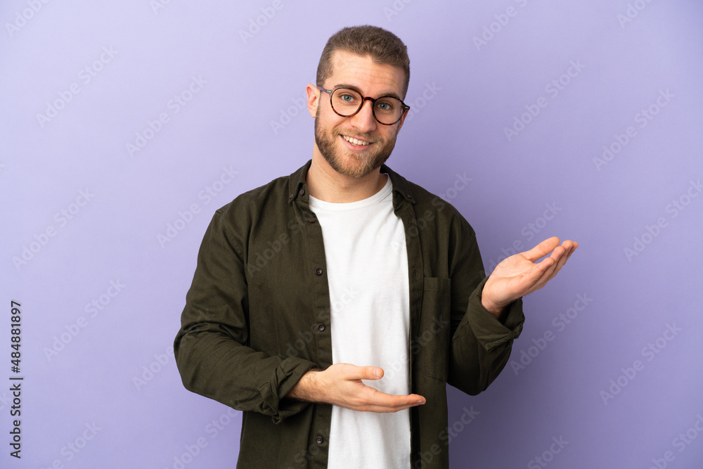 Young handsome caucasian man isolated on purple background extending hands to the side for inviting to come Young handsome caucasian man isolated on purple background extending hands to the side for inviting to come