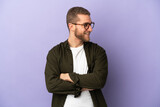 Young handsome caucasian man isolated on purple background looking to the side and smiling