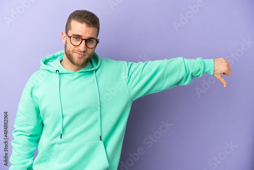 Young handsome caucasian man isolated on purple background showing thumb down with negative expression © luismolinero