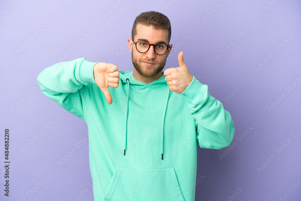 Young handsome caucasian man isolated on purple background making good-bad sign. Undecided between yes or not Young handsome caucasian man isolated on purple background making good-bad sign. Undecided between yes or not
