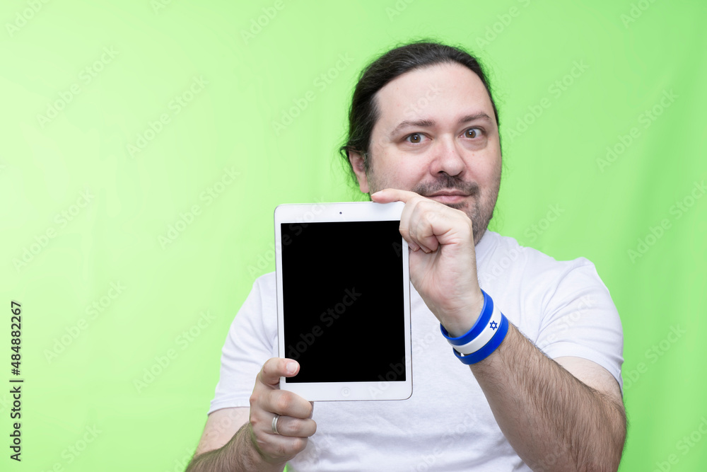 An adult man shows a blank tablet screen. Template with empty space on the screen. Selective focus on tablet. Bracelet in the colors of the flag of Israel. An adult man shows a blank tablet screen. Template with empty space on the screen. Selective focus on tablet. Bracelet in the colors of the flag of Israel.