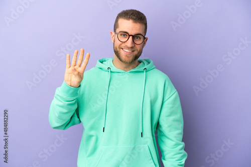 Young handsome caucasian man isolated on purple background happy and counting four with fingers © luismolinero