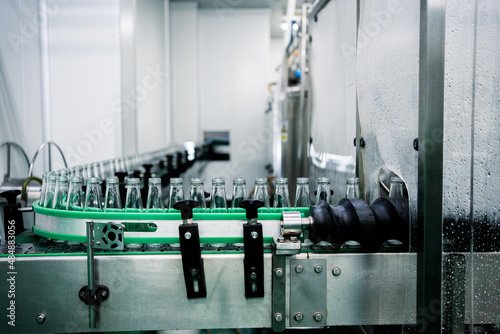 Photos Factory of production and packaging of herbal beverages, Many glass bottles on a conveyor belt enter the rinsing process Sterilize and fill herbal juice with a rotary automatic filling machine