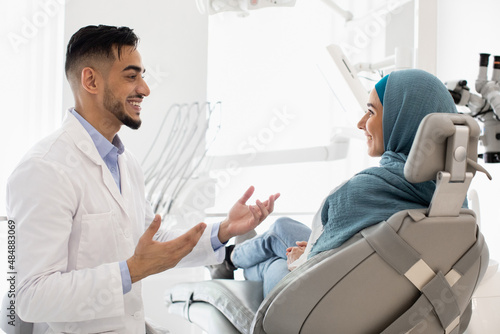 Handsome arab male dentist talking with muslim female patient at dental clinic