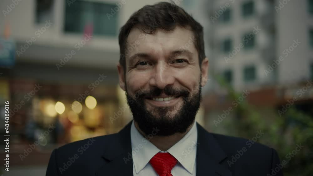Portrait business man in an expensive suit and a red tie, a handsome bearded senior businessman in the evening stands on the city streets next to a business building and looks into the camera, smiling Portrait business man in an expensive suit and a red tie, a handsome bearded senior businessman in the evening stands on the city streets next to a business building and looks into the camera, smiling