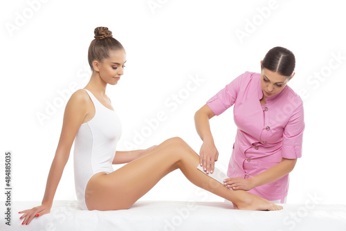 Beautician is removing hair from beautiful female body and legs with hot wax. Woman has a beauty treament procedure. Depilation, epilation, skin and health care concepts.