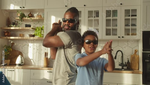 Cheerful good looking African father and adorable elementary age boy in sunglasses making flinger gun gesture, looking with friendly smiles, expressing carefree mood and happiness at home. photo