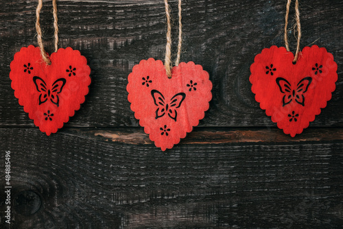 Three wooden hearts close-up hanging on dark wooden background. Valentine's Day.