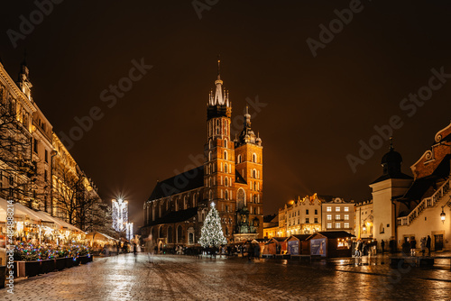 Krakow,Poland.Basilica of Saint Mary and famous Christmas market on main square,Rynek Glowny at night,decorated timber huts and Xmas tree.People enjoying festive atmosphere,blurred people in motion.