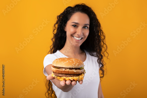 Happy Young Lady Holding And Giving Burger At Studio