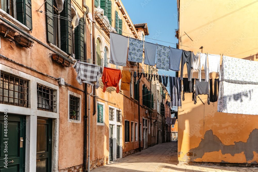 Laundry hanging out of typical Venetian facade,Italy.Narrow street with colorful buildings and clothes dry on rope,Venice.Clean clothes drying outdoors in small square.City lifestyle,urban scene.