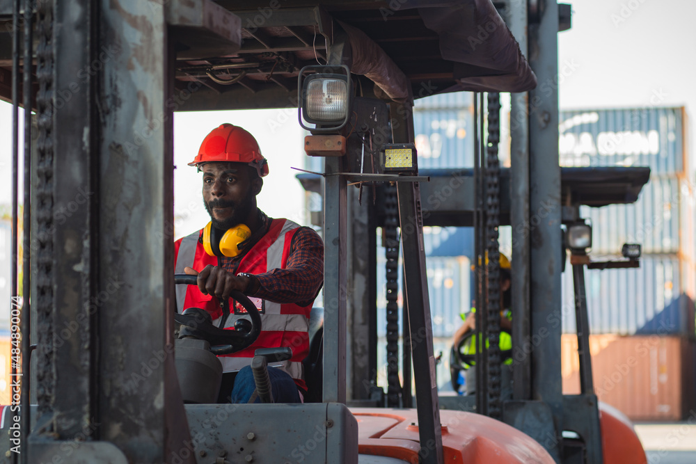 Male worker in uniform and helmet driving and operating on diesel container forklift truck at commercial dock site. Male worker in uniform and helmet driving and operating on diesel container forklift truck at commercial dock site.