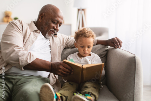 Fotografie African American Grandfather And Little Grandson Reading Book At Home
