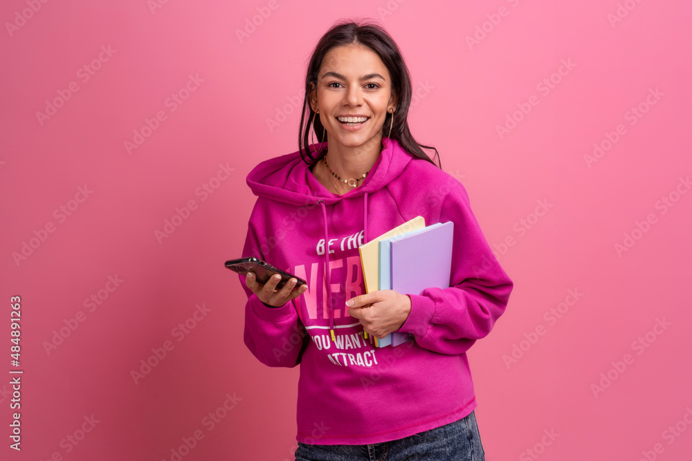 hispanic pretty woman in pink hoodie smiling holding holding notebooks and using smartphone hispanic pretty woman in pink hoodie smiling holding holding notebooks and using smartphone