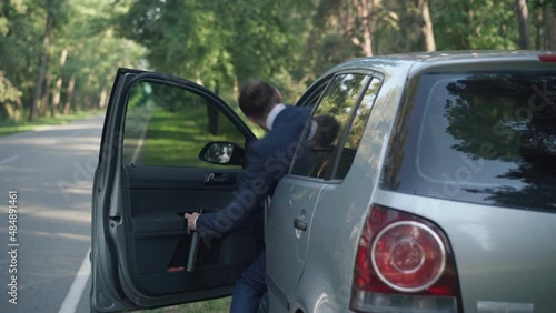 Back view drunken driver walking to car sitting on driver's seat closing door. Drunk young Caucasian man in suit driving drunk. Concept of illegal driving and traffic danger