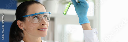 Woman scientist chemist looking at test tube with green liquid in laboratory