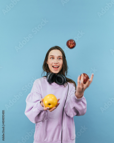 Foto Positive girl in headphones juggles apples on a blue background with a smile on his face