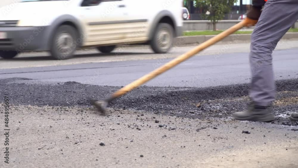A team of workers is looking for hot asphalt on the paths of the street - long-term care. Road workers level the asphalt with special shovels on the road in close-up. Road works in summer. A team of workers is looking for hot asphalt on the paths of the street - long-term care. Road workers level the asphalt with special shovels on the road in close-up. Road works in summer.