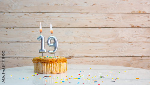 Happy birthday greetings for 19 years old from silver numbers against the background of white boards copy space. Beautiful birthday card with a muffin with a burning candle for nineteen years photo